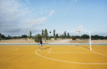 Joven lanzando bola negra en cancha de baloncesto amarilla al aire libre . - foto de stock