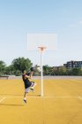 Young man playing on yellow basketball court outdoors. — Stock Photo