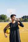 Junger Mann auf gelbem Basketballplatz trinkt Wasser aus Flasche. — Stockfoto
