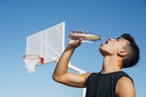 Junger Mann auf Basketballplatz trinkt Wasser aus Flasche. — Stockfoto
