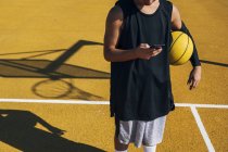 Basketballer nutzt Smartphone als Ruhepause nach Trainingseinheit. — Stockfoto