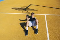 Male basketball player taking selfie with smartphone while lying on yellow court after training session. — Stock Photo