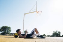 Мужчина баскетболист с помощью смартфона, лежащий на желтой корте после тренировки . — стоковое фото