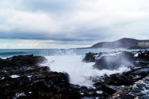Onde blu dell'oceano con texture in schiuma bianca contro le rocce — Foto stock