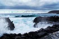 Ondas azules del océano con textura de espuma blanca contra rocas. - foto de stock