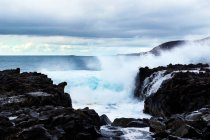 Onde blu dell'oceano con texture in schiuma bianca contro le rocce — Foto stock