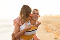 Веселый мужчина катает на спине улыбающуюся женщину на курорте — стоковое фото