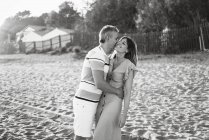 Взрослые мужчины и женщины смеются и обнимаются, веселясь на песчаном берегу курорта — стоковое фото
