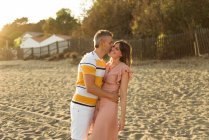 Homem adulto animado beijando mulher enquanto rindo e abraçando uns aos outros enquanto se divertem na costa arenosa no resort — Fotografia de Stock