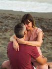 Mann und Frau lächeln und umarmen sich, während sie auf Sand am Meer sitzen und sich beim Date entspannen — Stockfoto