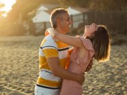 Homem e mulher adultos excitados rindo e abraçando um ao outro enquanto se divertindo na costa arenosa no resort — Fotografia de Stock