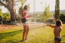 Aufgeregt Teenie-Mädchen lachen und spielen mit Strahl sauberen Wassers, während Spaß im Garten an einem sonnigen Tag — Stockfoto