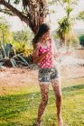 Emocionado adolescente riendo y jugando con chorro de agua limpia mientras se divierten en el jardín en el día soleado - foto de stock
