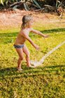 Full body shirtless little girl in panties playing under drops of clean water while having fun on lawn in yard on sunny summer day — Stock Photo