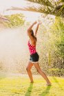 Eccitato teen girl ridendo e giocando con getto d'acqua pulita mentre si diverte in giardino nella giornata di sole — Foto stock