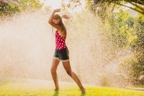 Excited teen girl laughing and playing with jet of clean water while having fun in garden on sunny day — Stock Photo
