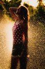 Возбужденная девочка-подросток смеется и играет с струей чистой воды, веселясь в саду в солнечный день — стоковое фото