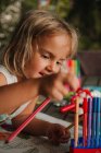 Menina focada inclinando-se na mesa e colorir fotos no livro com caneta marcador no fundo borrado do quarto em casa — Fotografia de Stock