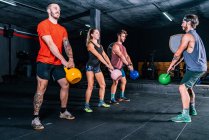 Companheiros musculares com treinador levantando sinos chaleira enquanto o treinamento funcional no health club contemporâneo — Fotografia de Stock