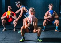 Companheiros musculares com treinador levantando sinos chaleira enquanto o treinamento funcional no health club contemporâneo — Fotografia de Stock