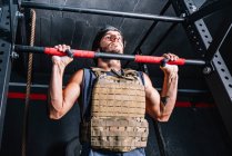 Strong man doing pull-up exercise with weight on horizontal bar — Stock Photo