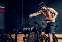 Strong man training on contemporary exercise bike in sport club — Stock Photo