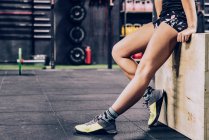 Cultiver femme fatiguée en vêtements de sport relaxant dans la salle de gym sur fond flou — Photo de stock