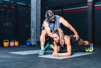 Ernste verschwitzte muskulöse Instruktor hilft, Bauchmuskeln im Fitnessstudio durchführen — Stockfoto