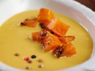 Крупный план вкусного имбирного и апельсинового сливочного супа с кусочками жареной тыквы — стоковое фото