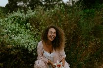 Lächelnde Frau berührt Blume im Wald — Stockfoto