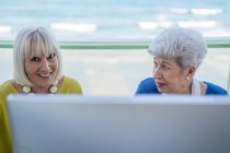 Stylish old friends sitting at table with computer on balcony on resort — Stock Photo