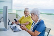 Stylish old friends browsing social media on tablet while sitting at table with computer on balcony on resort — Stock Photo