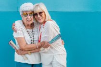Positive trendy grey-haired women with big color hand fans hugging — Stock Photo