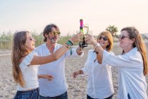 Alegre maduro padres y jóvenes hijas tintineo vasos de vino y riendo mientras se celebra la reunión familiar por la noche en el resort - foto de stock