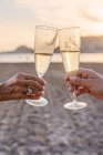 Mãe e filha irreconhecíveis batendo taças de vinho e propondo brinde enquanto comemoram a reunião familiar na praia de areia à noite — Fotografia de Stock