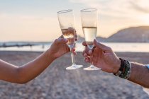 Unrecognizable mother and daughter clinking goblets of wine and proposing toast while celebrating family reunion on sandy beach in evening — Stock Photo