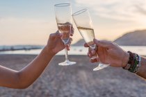 Mãe e filha irreconhecíveis batendo taças de vinho e propondo brinde enquanto comemoram a reunião familiar na praia de areia à noite — Fotografia de Stock