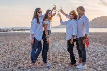 Веселые зрелые родители и молодые дочери звонят бокалы вина и смеются во время празднования воссоединения семьи вечером на курорте — стоковое фото