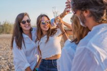 Cheerful mature parents and young daughters clinking glasses of wine and laughing while celebrating family reunion in evening on resort — Stock Photo