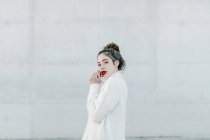 Вид збоку молодої жіночої моделі в стильному теплому затишному светрі, який дивиться в камеру, стоячи на сірій стіні на міській вулиці — стокове фото