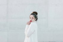 Vista laterale del giovane modello femminile in elegante caldo maglione accogliente guardando in basso mentre in piedi contro il muro grigio sulla strada della città — Foto stock