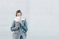 Молода жінка вкрита теплим шарфом, дивлячись далеко, стоячи навпроти стіни на міській вулиці — стокове фото