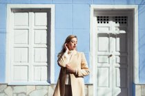 Молода леді в елегантній блузці з закритими очима, що стоять біля білих дверей і вікна синьої будівлі на вулиці — стокове фото