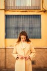 Чуттєва молода жінка з довгим волоссям, стильне пальто і дивиться вниз, стоячи за межами будівлі на вулиці міста — стокове фото