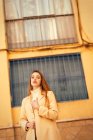 Чуттєва молода жінка з довгим волоссям, стильне пальто і дивиться в камеру, стоячи на вулиці будівлі на міській вулиці — стокове фото