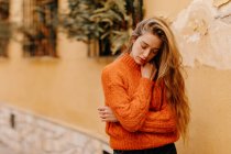 Чуттєва молода жінка в модному в'язаному светрі торкається підборіддя з закритими очима будинок з горщиками рослин — стокове фото