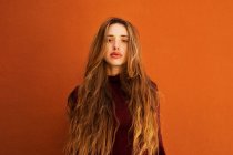 Portrait de jeune femme séduisante aux cheveux longs regardant en caméra contre un mur orange sur la rue — Photo de stock