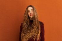 Портрет привлекательной молодой женщины с длинными волосами, смотрящей в камеру напротив оранжевой стены на улице — стоковое фото