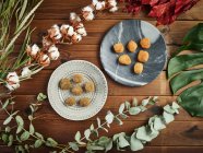 From above branches and leaves of various plants arranged around plates with tasty croquettes on timber tabletop — Stock Photo