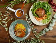 Vista dall'alto della gamba della lampada ripiena servita su piatti con verdure fresche e riso in mezzo a ramoscelli verdi sul tavolo di legno — Foto stock